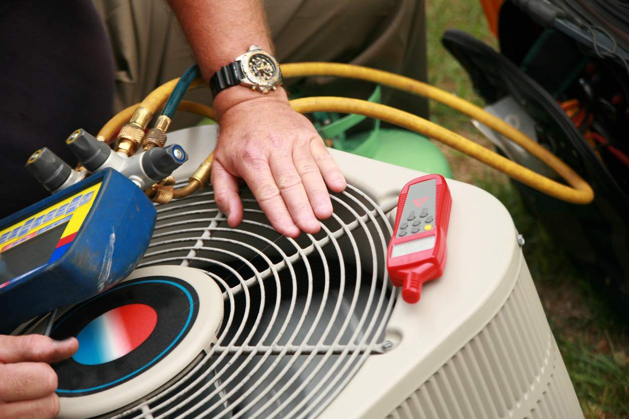 Person checking air conditioner unit with gauges and tools outdoors.