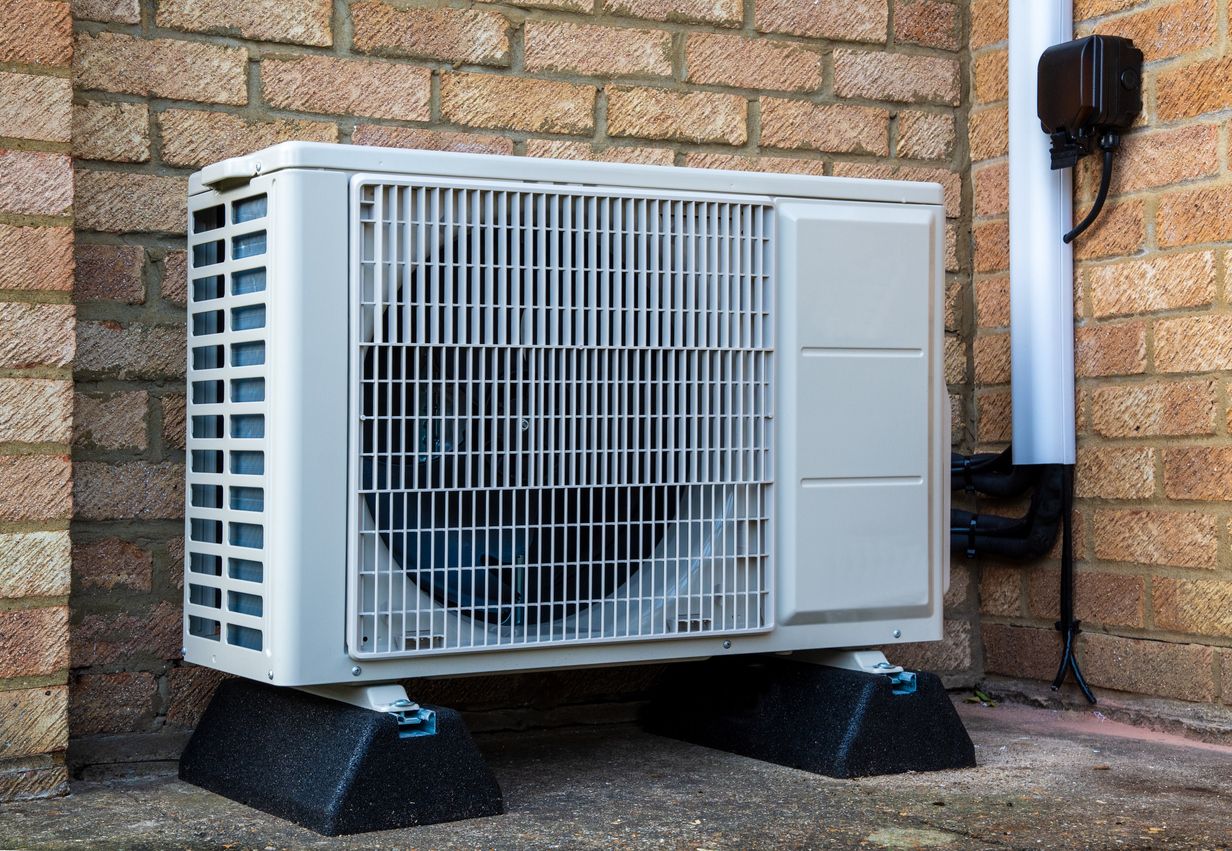 Outdoor heat pump unit installed against brick wall for efficient heating and cooling.